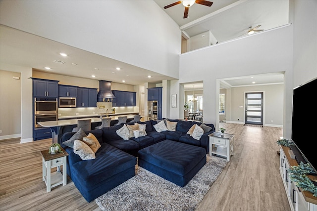 living area with baseboards, recessed lighting, a towering ceiling, and light wood-style floors