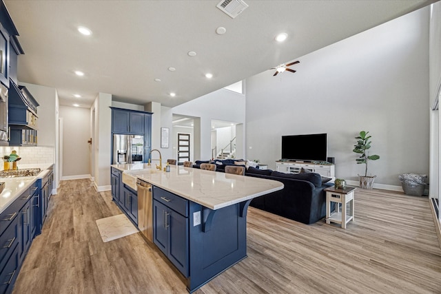 kitchen with appliances with stainless steel finishes, a large island with sink, blue cabinetry, and a breakfast bar area