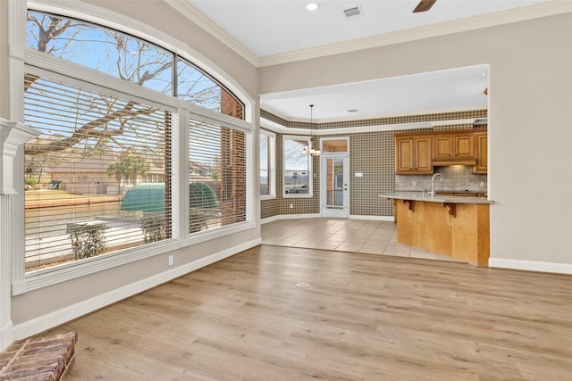 kitchen featuring a breakfast bar, decorative light fixtures, tasteful backsplash, ornamental molding, and light hardwood / wood-style floors