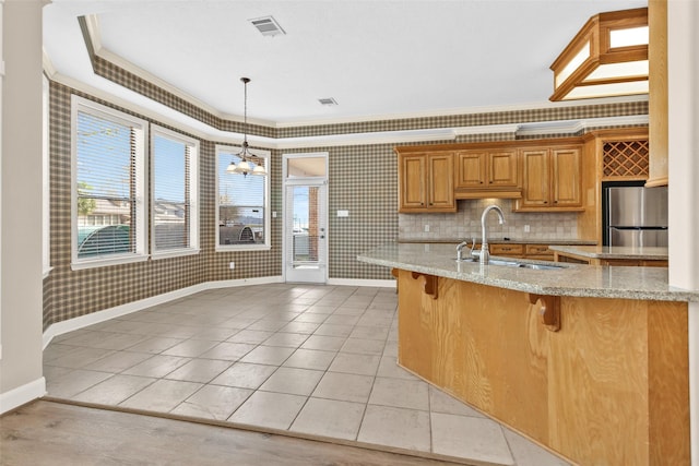 kitchen with sink, stainless steel fridge, hanging light fixtures, light stone countertops, and a kitchen bar