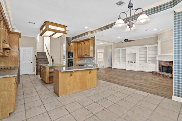 kitchen with ceiling fan with notable chandelier, a kitchen breakfast bar, black appliances, crown molding, and a brick fireplace