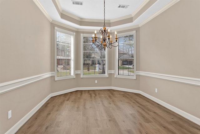 unfurnished dining area with a raised ceiling, ornamental molding, hardwood / wood-style floors, and an inviting chandelier