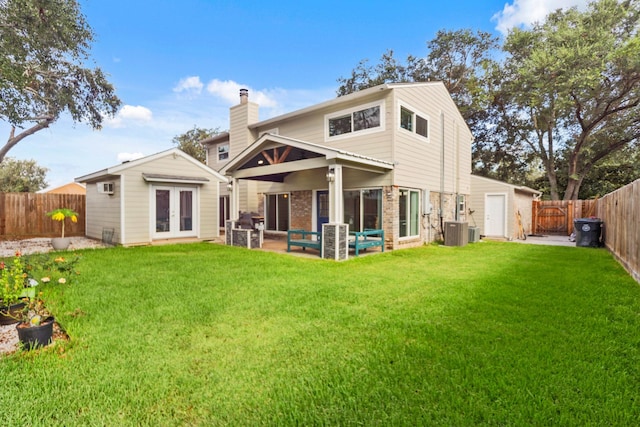 rear view of property with a lawn, french doors, an outbuilding, central AC unit, and a patio area