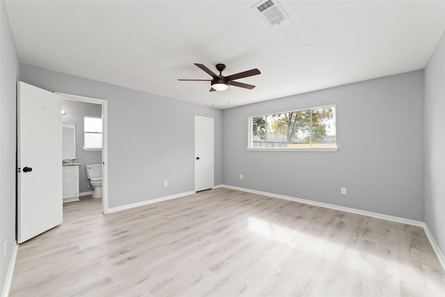 unfurnished bedroom with multiple windows, ceiling fan, ensuite bath, and light hardwood / wood-style flooring