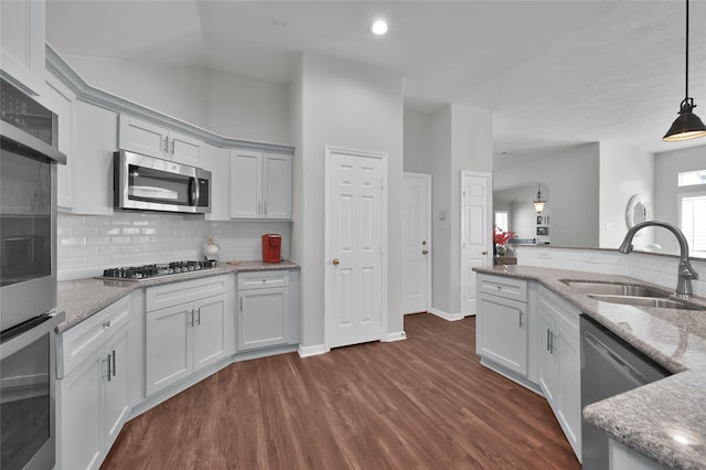 kitchen featuring appliances with stainless steel finishes, pendant lighting, sink, light stone counters, and dark wood-type flooring