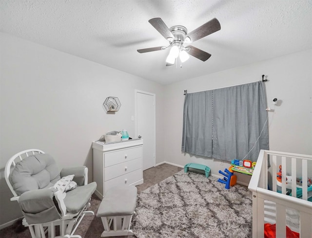 bedroom featuring ceiling fan, a crib, a textured ceiling, and dark colored carpet