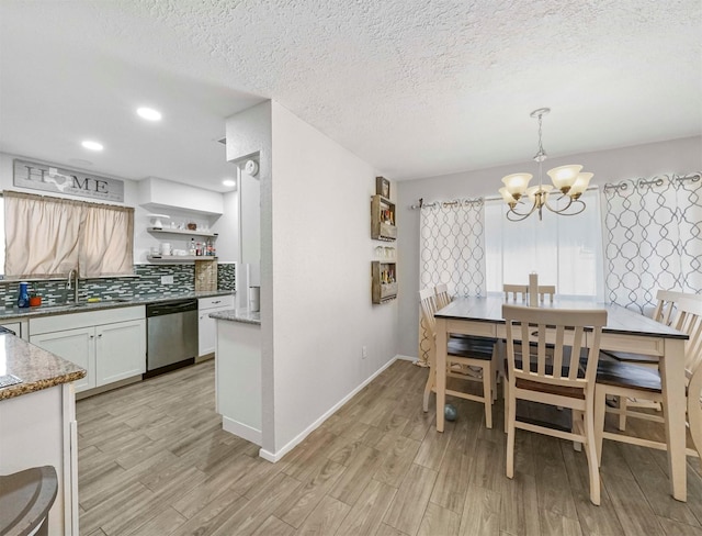 dining space with a notable chandelier, sink, a textured ceiling, and light wood-type flooring