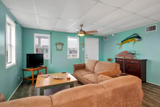 living room with a drop ceiling, dark wood-type flooring, and ceiling fan