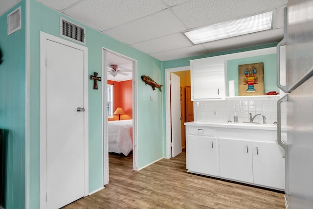 interior space with refrigerator, backsplash, white cabinets, a drop ceiling, and light wood-type flooring