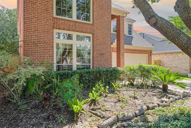 exterior space with an attached garage, brick siding, and a shingled roof