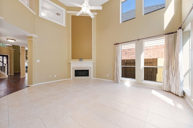 unfurnished living room featuring light tile patterned flooring, ceiling fan, a premium fireplace, and ornate columns