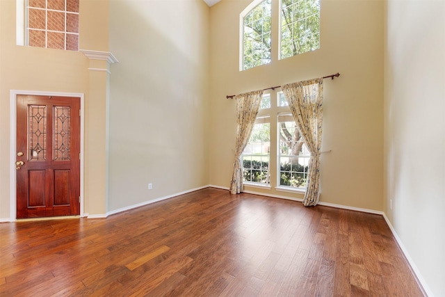 foyer entrance with hardwood / wood-style flooring, decorative columns, and a high ceiling