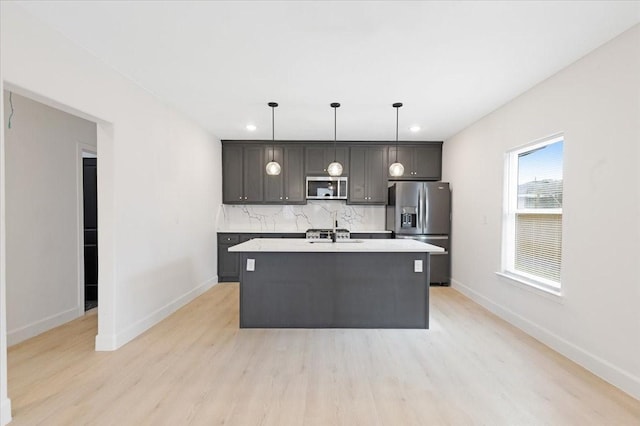6609 Ave Q, Houston, TX 77011 - kitchen with light wood finished floors, decorative backsplash, appliances with stainless steel finishes, a kitchen island with sink, and light countertops