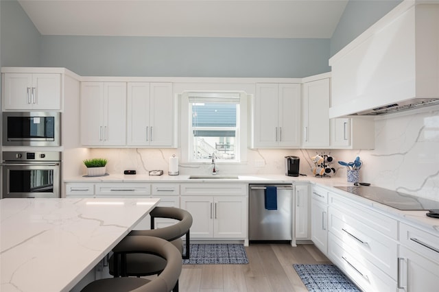 kitchen with sink, appliances with stainless steel finishes, custom range hood, decorative backsplash, and white cabinets