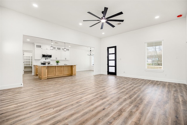 unfurnished living room featuring ceiling fan with notable chandelier and light hardwood / wood-style floors