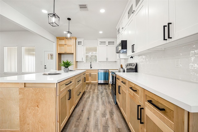 kitchen featuring appliances with stainless steel finishes, hanging light fixtures, a center island, light hardwood / wood-style floors, and decorative backsplash