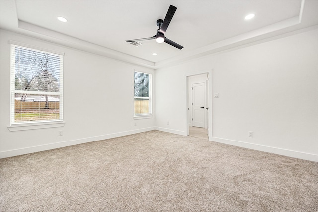 spare room with ceiling fan, light colored carpet, and a tray ceiling