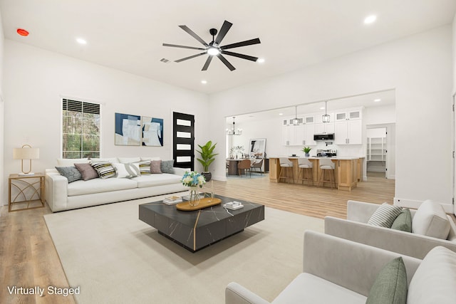 living room with ceiling fan with notable chandelier and light hardwood / wood-style flooring