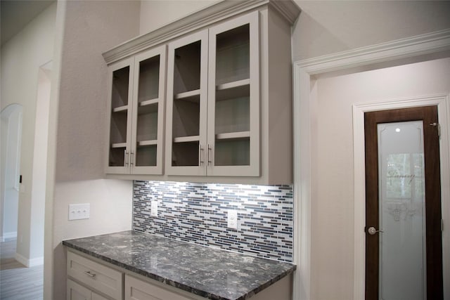kitchen featuring dark stone counters, backsplash, and glass insert cabinets