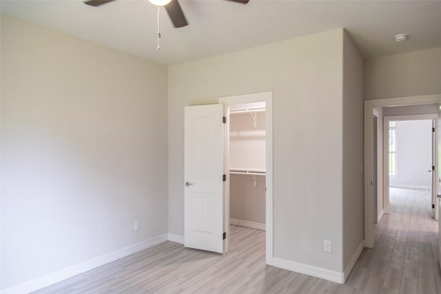 unfurnished bedroom with baseboards, a ceiling fan, a spacious closet, light wood-style floors, and a closet