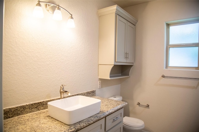 bathroom featuring a textured wall, vanity, and toilet