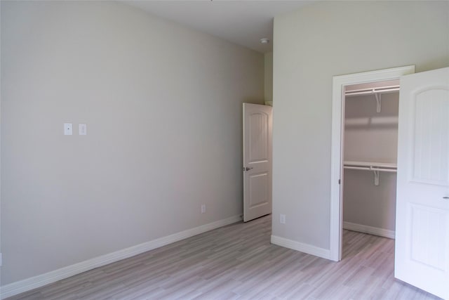 unfurnished bedroom featuring a walk in closet, a closet, light wood finished floors, and baseboards