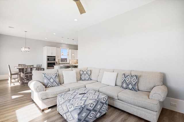 living room featuring ceiling fan with notable chandelier and light hardwood / wood-style floors