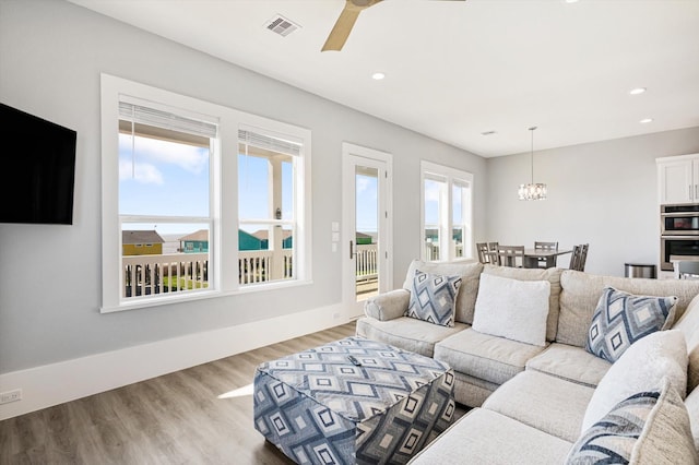 living room with ceiling fan with notable chandelier and light hardwood / wood-style floors