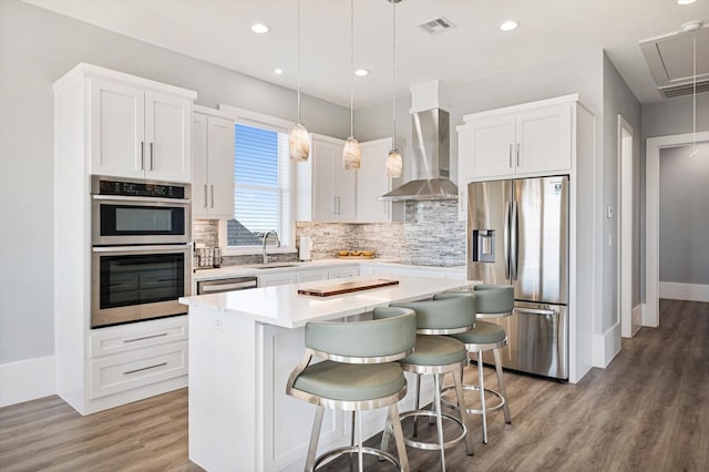 kitchen featuring a kitchen island, a breakfast bar, hanging light fixtures, stainless steel appliances, and wall chimney range hood