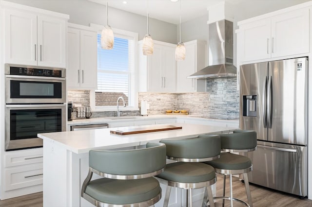 kitchen with a kitchen bar, wall chimney range hood, a kitchen island, stainless steel appliances, and white cabinets