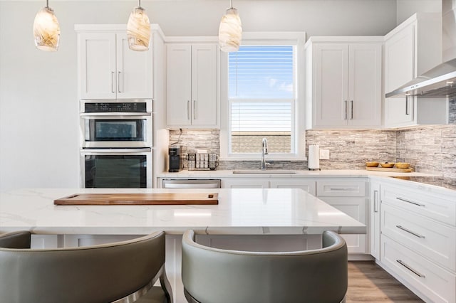 kitchen featuring white cabinetry, decorative light fixtures, and wall chimney exhaust hood