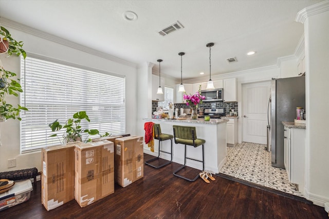 kitchen featuring decorative light fixtures, white cabinetry, wood-type flooring, backsplash, and stainless steel appliances