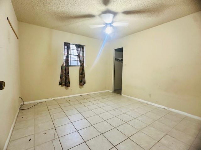 tiled empty room featuring ceiling fan and a textured ceiling