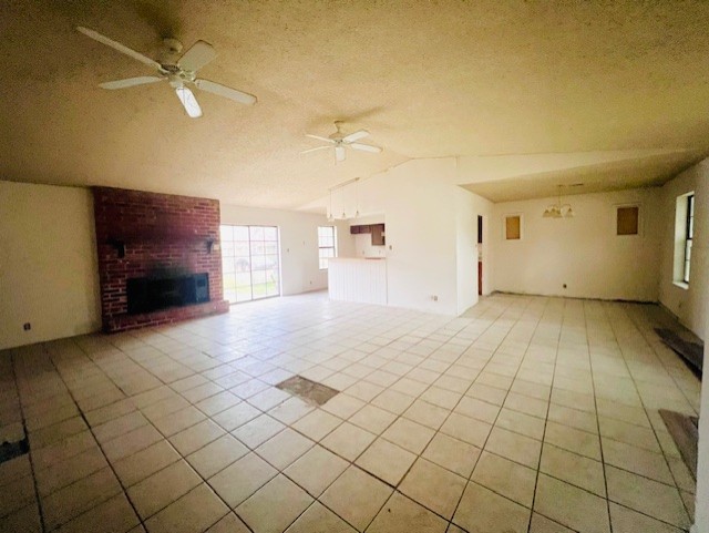 unfurnished living room with ceiling fan, a fireplace, vaulted ceiling, and light tile patterned floors