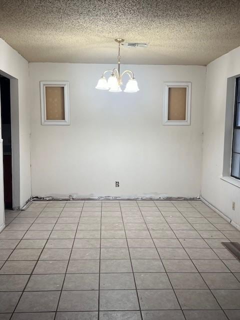 spare room with a chandelier, a textured ceiling, and light tile patterned floors