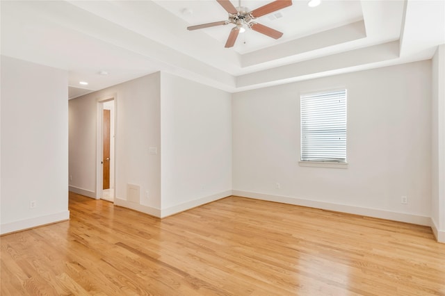 spare room featuring a raised ceiling, ceiling fan, and light wood-type flooring