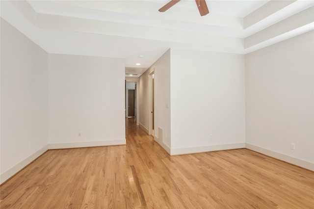 unfurnished room with ceiling fan, a tray ceiling, and light hardwood / wood-style flooring