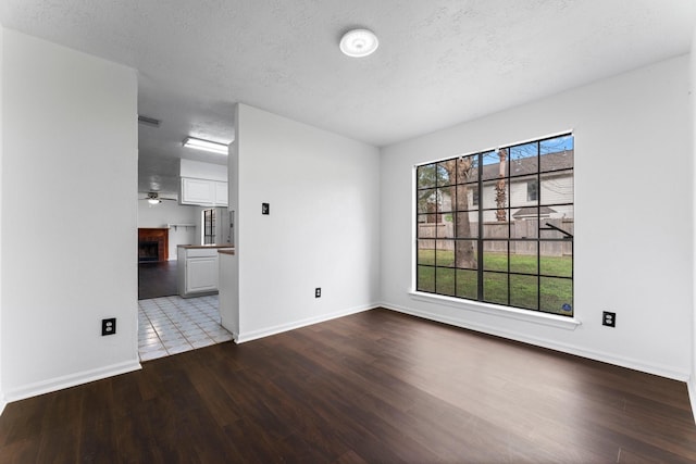 spare room with ceiling fan, a fireplace, a textured ceiling, and light wood-type flooring