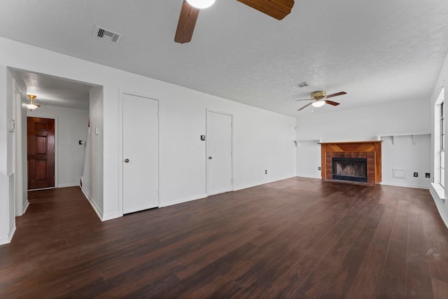 unfurnished living room with a tile fireplace, dark wood-type flooring, a textured ceiling, and ceiling fan