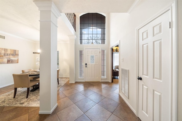 foyer entrance featuring decorative columns, visible vents, baseboards, ornamental molding, and a high ceiling