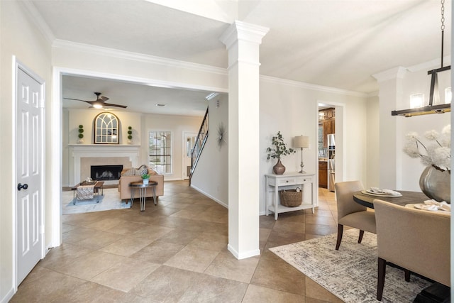 foyer with crown molding, a premium fireplace, a ceiling fan, baseboards, and ornate columns