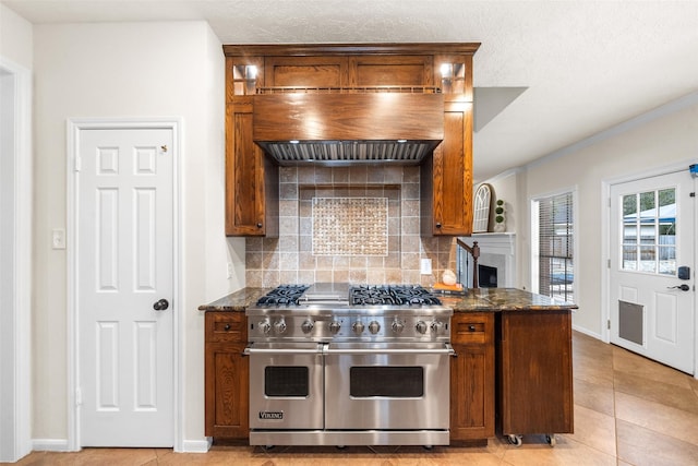 kitchen featuring tasteful backsplash, range with two ovens, dark stone countertops, premium range hood, and a fireplace