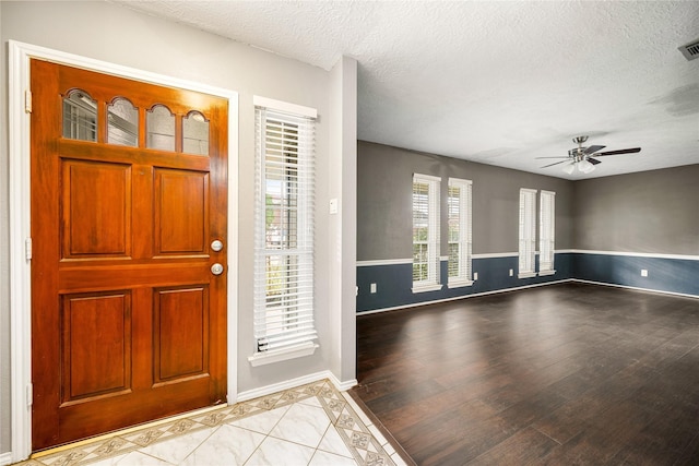 foyer entrance with ceiling fan, a textured ceiling, and light wood-type flooring