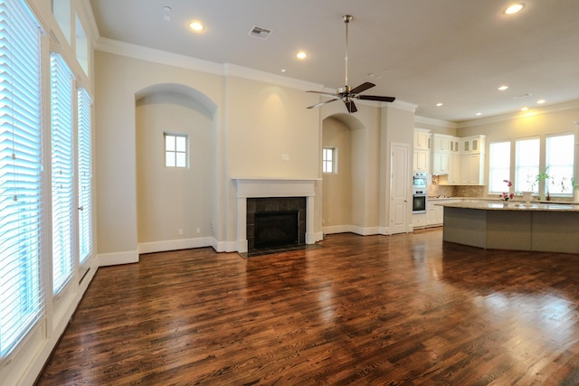 unfurnished living room featuring a tile fireplace, plenty of natural light, dark wood-type flooring, and ornamental molding