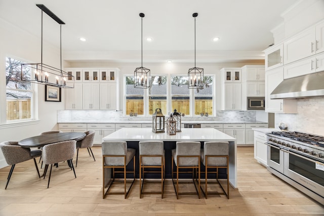 kitchen with under cabinet range hood, a kitchen bar, light countertops, stainless steel appliances, and white cabinetry