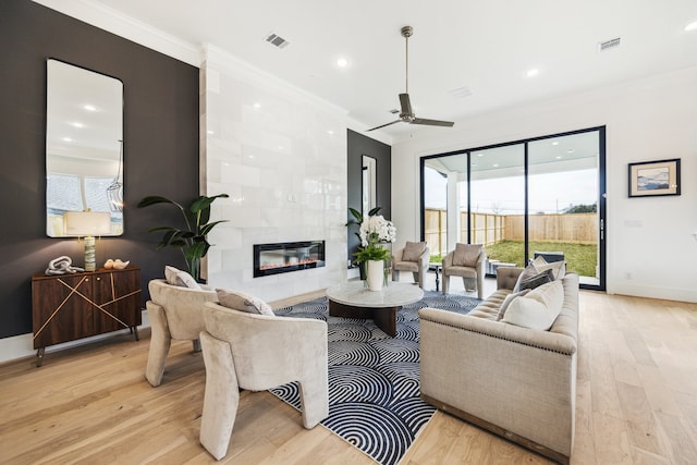 living room with a tiled fireplace, crown molding, ceiling fan, and light hardwood / wood-style floors