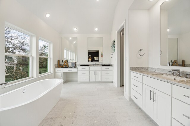 bathroom featuring lofted ceiling, a freestanding tub, two vanities, a sink, and marble finish floor