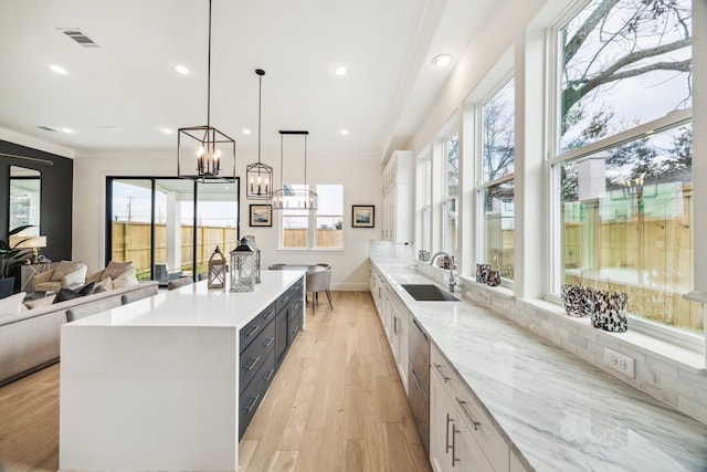 kitchen featuring light wood finished floors, a spacious island, visible vents, ornamental molding, and a sink