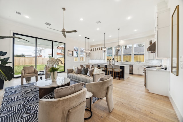 living area featuring visible vents, a healthy amount of sunlight, ornamental molding, and light wood finished floors