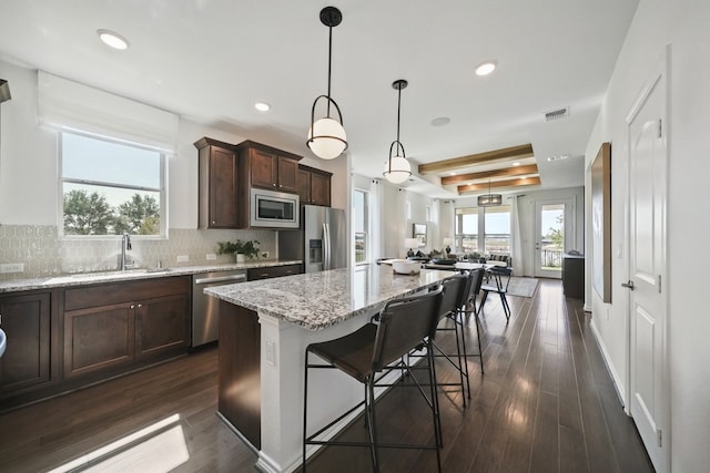 kitchen with appliances with stainless steel finishes, hanging light fixtures, a breakfast bar area, light stone counters, and a tray ceiling